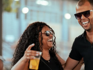 Duas pessoas sorrindo e se abraçando enquanto seguram bebidas no Circuito Gastronômico de Favelas.